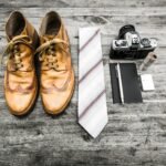 pair of brown leather boots beside necktie next to pen, notebook, and MILC camera